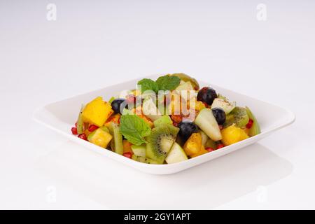 Salade de fruits mélangée préparée dans une vaisselle blanche et garnie de feuilles de menthe. Banque D'Images