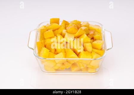 Cubes de mangue mûrs ou morceaux coupés disposés dans un récipient carré en verre avec fond blanc. Banque D'Images