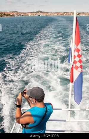 Vodice, Croatie - 25 août 2021 : un homme debout sur le dos d'un navire prenant des photos sur un téléphone portable et un drapeau croate Banque D'Images