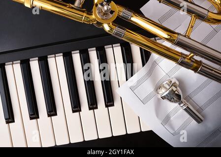 Le concept de concert de trombone et de piano avec fond de trombone sur piano et feuilles de personnel.Vue de dessus.Composition horizontale. Banque D'Images