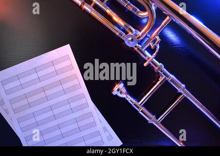 Trombone de jazz avec draps de personnel vides illuminés avec des lumières de couleur sur une table noire.Vue de dessus.Composition horizontale. Banque D'Images
