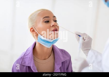 Diagnostic du coronavirus.Infirmière effectuant un test PCR Covid-19 pour jeune femme à l'aide d'un écouvillon stérile, assis sur un mur blanc Banque D'Images
