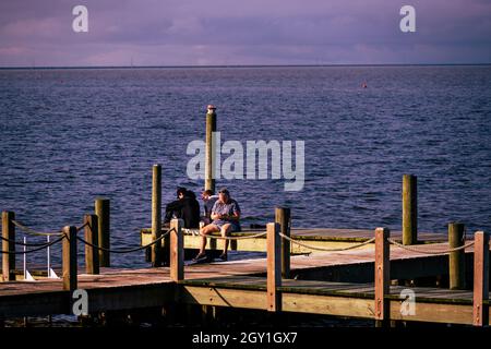 Duck, Caroline du Nord, États-Unis -- 8 août 2021.Un homme et deux femmes s'assoient sur un quai au-dessus de Currituck Sound, à Duck, en Caroline du Nord. Banque D'Images