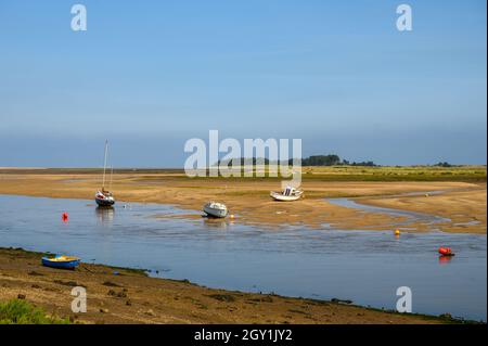 Bateaux assis sur le lit de la rivière à marée basse sur la rivière East Fleet avec des collines boisées de l'est au loin à Wells Next the Sea, Norfolk, Angleterre. Banque D'Images