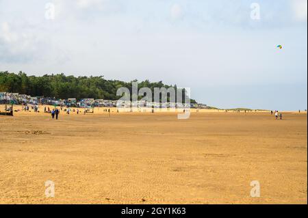 Personnes appréciant la vie de plage avec des huttes de plage et des bois en arrière-plan, Wells Next the Sea, Norfolk, Angleterre. Banque D'Images