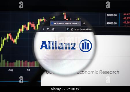 Le logo de la société Allianz sur un site Web présentant des développements flous sur le marché boursier en arrière-plan, vu sur un écran d'ordinateur à travers une loupe Banque D'Images