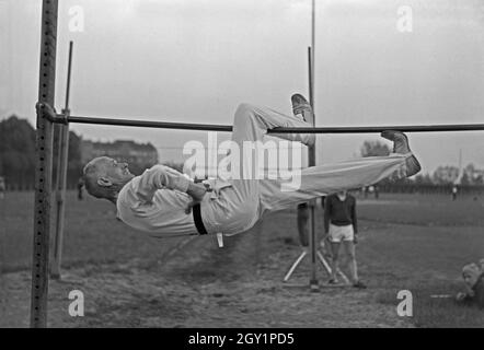 Ein Turner aus der Altherrenriege Balanceübung Turnvereins von der trägt suis vor Reck, Deutschland 1930er Jahre. Un membre de la haute direction du ministère d'un gymnastic club d'effectuer un exercice d'équilibre à un bar sur un terrain de sport, de l'Allemagne des années 1930. Banque D'Images