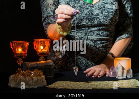 Détail des mains d'une femme passant un pendule sur un jeu de cartes de tarot.Concept d'une session de divination avec des cartes de tarot. Banque D'Images