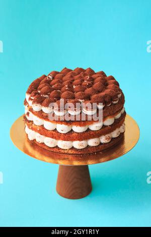 Gâteau d'anniversaire sur le support à gâteau en bois.Magnifique génoise au chocolat avec crème fouettée garnie de cacao saupoudré.Arrière-plan bleu.Copier l'espace Banque D'Images