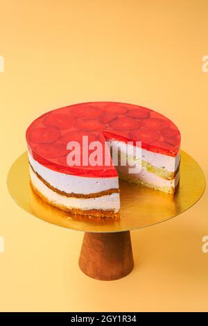 Gâteau d'anniversaire en tranches décoré de gelée rouge et de fraises sur le support à gâteau en bois.Magnifique gâteau éponge à la crème fouettée.Fond jaune Banque D'Images