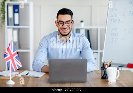Joyeux tuteur masculin ayant appel vidéo avec les étudiants sur ordinateur portable, donnant la leçon d'anglais sur le Web de la maison Banque D'Images