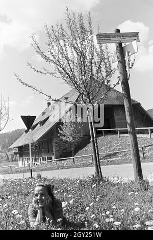 Eine junge Frau auf einer Wiese vor einem alten Haus im Schwarzwald, Deutschland 1930er Jahre. Une jeune femme couchée sur une prairie en face d'une vieille maison à la Forêt-Noire, Allemagne 1930. Banque D'Images