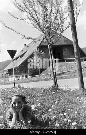 Eine junge Frau auf einer Wiese vor einem alten Haus im Schwarzwald, Deutschland 1930er Jahre. Une jeune femme couchée sur une prairie en face d'une vieille maison à la Forêt-Noire, Allemagne 1930. Banque D'Images