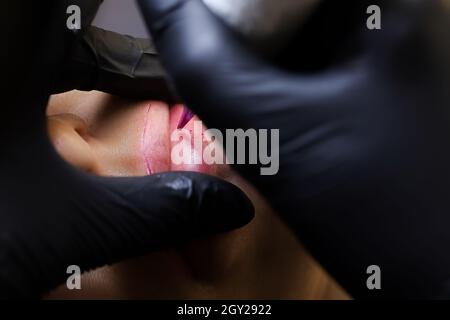 l'artiste maître de tatouage étire les lèvres du modèle avec deux doigts et met ensuite un tatouage sur ses lèvres Banque D'Images