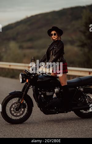 Moto élégante femme en mini jupe, veste en cuir sur moto de style vintage.Le conducteur séduisant des bottes de protection sur route.Trajet Banque D'Images