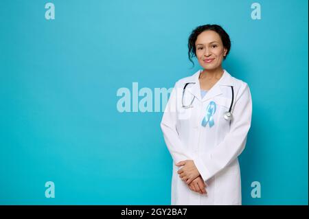 Portrait de la belle femme médecin en robe médicale blanche avec ruban de conscience bleu, symbole de la Journée mondiale du diabète, sourires regardant la caméra posant ag Banque D'Images