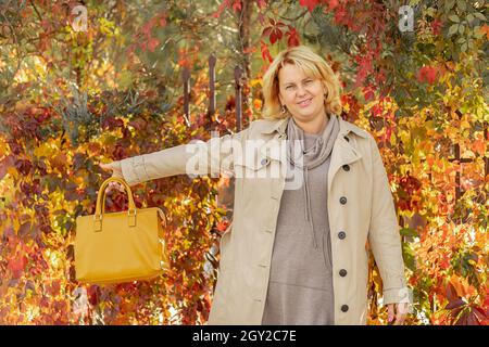 une jeune femme vêtue de vêtements décontractés, vêtue d'un manteau beige, tient le sac jaune sur le fond du feuillage d'automne Banque D'Images