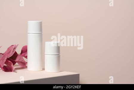 deux tubes en plastique blanc vides pour cosmétiques sont placés sur un podium en bois sur un fond beige avec une ombre.Récipients pour crèmes, shampooings, sous-produits liquides Banque D'Images