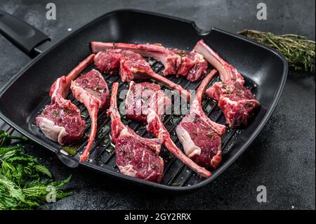 Prêt à cuire de l'agneau cru, le mouton croque des steaks dans une casserole avec des herbes. Arrière-plan noir. Vue de dessus Banque D'Images