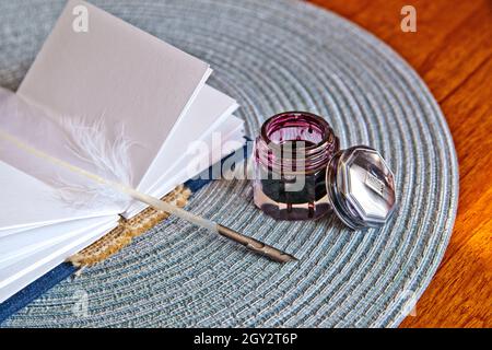 Petit livre de journal et plume blanche quill reposent sur un platemat à côté d'un pot d'encre ouvert Banque D'Images