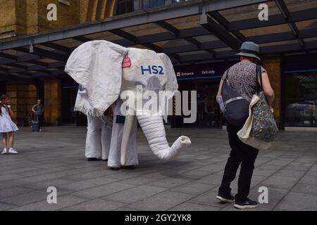 Londres, Royaume-Uni.5 août 2021.Les manifestants portant un costume d'éléphant blanc « HS2 » sont conduits à l'extérieur de la gare par un autre manifestant.Des militants se sont rassemblés devant la gare de King's Cross pour protester contre le nouveau système ferroviaire High Speed 2 (HS2), qui selon les écologistes sera « écologiquement dévastateur » et coûtera aux contribuables 170 milliards de livres sterling. Banque D'Images