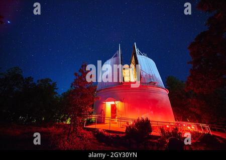 Observatoire éclairé en bleu et rouge la nuit entouré d'arbres Banque D'Images