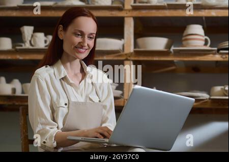 Une jeune femme assise à l'ordinateur portable dans un atelier de poterie Banque D'Images