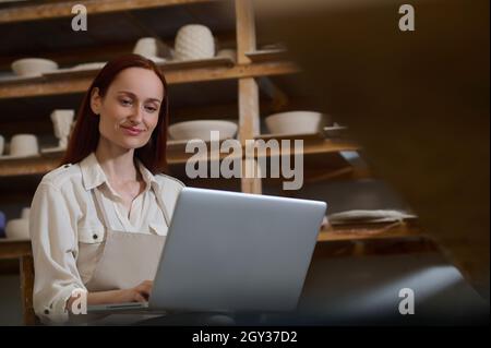 Une jeune femme assise à l'ordinateur portable dans un atelier de poterie Banque D'Images
