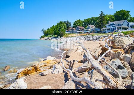 Bois de Driftwood et rochers sur une plage de sable avec des maisons de lac en arrière-plan Banque D'Images