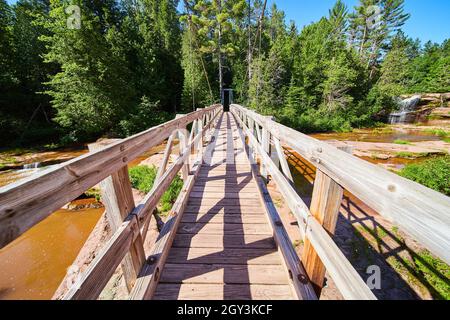 Marche sur le pont suspendu au-dessus de la rivière brune avec chute d'eau à distance Banque D'Images