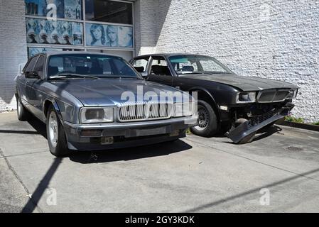 Deux voitures épaves devant un magasin.Les deux modèles sont des modèles Jaguar XJ (XJ40), bien que l'un semble être une variante double six à emblème Daimler. Banque D'Images