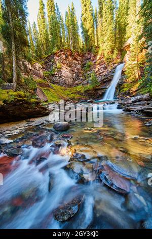 Vue sur un lit de rivière peu profond avec une magnifique cascade au loin dans un canyon coloré de mousse Banque D'Images
