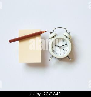 Papier mémo vierge, crayon, horloge sur fond blanc. Vue du dessus, espace de copie Banque D'Images