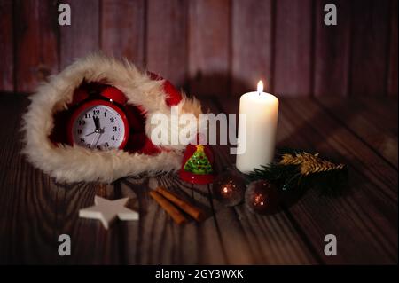 Horloge rouge dans chapeau de Santa avec branche de pin, bougie, boules et étoile sur fond de bois - concept de Noël Banque D'Images