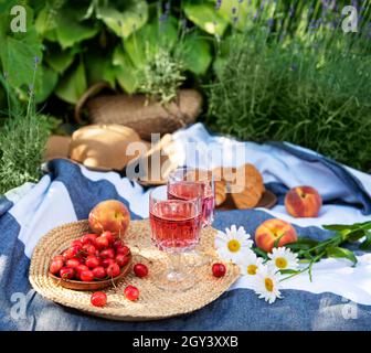 Pique-nique en plein air dans les champs de lavande. Vin de rose dans un verre, cerises et chapeau de paille sur la couverture Banque D'Images