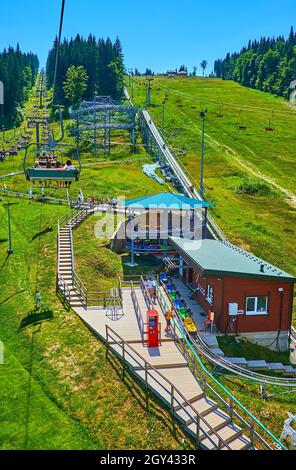 Le télésiège surmonte la pente verte du mont Bukovel avec une vue sur l'attraction Speed Fun rodelbahn et la forêt d'épicéa en arrière-plan, en Ukraine Banque D'Images