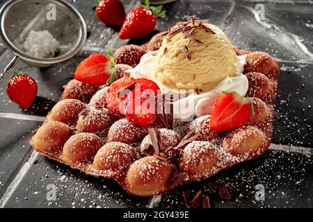 Dessert d'été gastronomique avec gaufres à bulles, fraises fraîches, crème fouettée et glace aux baies fruitées, nappée de chocolat en flocons et de sucre glace Banque D'Images