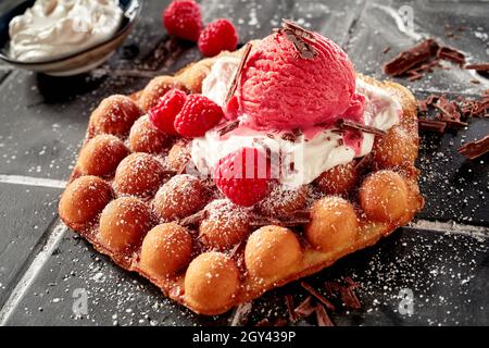 Délicieuse gaufre à bulles recouverte de crème glacée à la framboise et de baies rouges mûres fraîches garnies de flocons de chocolat sur un lit de crème fouettée Banque D'Images