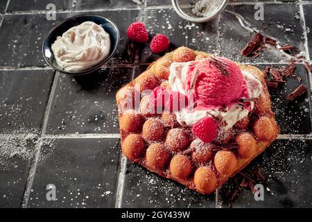 Délicieuse gaufre à la framboise avec une dose de crème fouettée et une glace fruitée aux baies de saison, garnie de flocons de chocolat et arrosée d'ic Banque D'Images