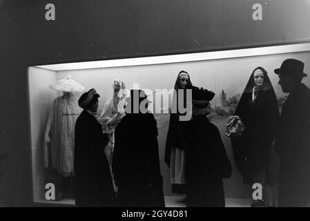 Messebesucher vor einem Schaukasten mit landestypischen Trachten, anlässlich der Wiener Modewoche im Haus der mode ' Palais Lobkowitz', Deutschland 1940er Jahre.Visiteurs à une foire devant une vitrine avec des costumes traditionnels, à l'occasion de la Wiener Modewoche dans la maison de la mode ' Palais Lobkowitz', Allemagne des années 1940. Banque D'Images