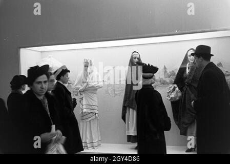 Messebesucher vor einem Schaukasten mit landestypischen Trachten, anlässlich der Wiener Modewoche im Haus der mode ' Palais Lobkowitz', Deutschland 1940er Jahre.Visiteurs à une foire devant une vitrine avec des costumes traditionnels, à l'occasion de la Wiener Modewoche dans la maison de la mode ' Palais Lobkowitz', Allemagne des années 1940. Banque D'Images