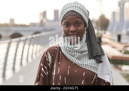 Portrait d'une jeune femme africaine vêtue de musulmans souriant à l'appareil photo tout en se tenant debout à l'extérieur Banque D'Images