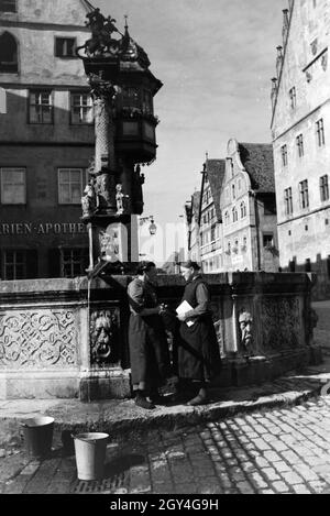 Zwei Frauen verwalten sich während Sie die Wassereimer mit Wasser aus dem Springbrunnen vor dem Rathaus imposanten voll laufen lassen, Rothenburg ob der Tauber, Allemagne Allemagne Années 1930 er Jahre. Deux femmes ayant un chat tandis que le bucktes sont remplissage avec de l'eau hors de la fontaine placée en face de l'impressionnant hôtel de ville de Rothenburg ob der Tauber, Allemagne 1930. Banque D'Images