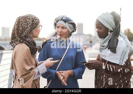 Groupe de femmes musulmanes utilisant leur téléphone mobile et discutant d'applications en ligne en étant debout dans la ville Banque D'Images