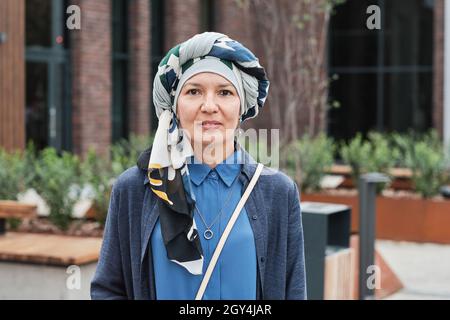 Portrait d'une élégante femme mûre dans hijab souriant à l'appareil photo tout en se tenant dans la rue Banque D'Images