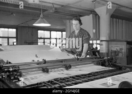 Eine Druckereimitarbeiterin Papierbögen bedruckten high die eine dans Planschneidemaschine Maschinenbaukonzern produziert vom Maschinenfabrik Augsburg-Nürnberg (homme), Deutschland 1930 er Jahre. Un travailleur dans une imprimerie met le papier imprimé à l'intérieur d'une machine à couper les feuilles, qui est produite par la société d'ingénierie mécanique (homme), Maschinenfabrik Augsburg-Nürnberg Allemagne 1930. Banque D'Images