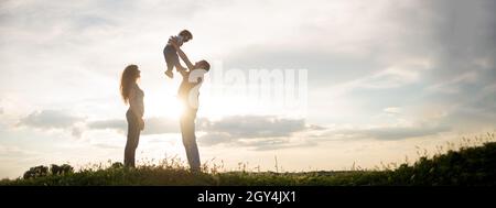 une mère de famille, un père et un petit fils, marchent au coucher du soleil.Silhouettes de parents et de tout-petits enfants sur le fond du ciel.Liberté et style de vie actif Banque D'Images