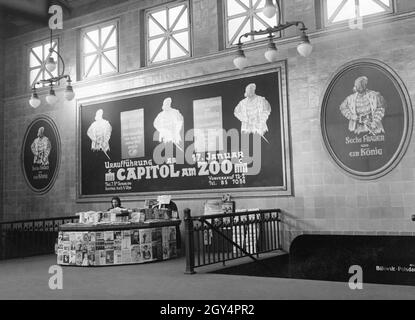 « une jeune femme se trouve derrière son kiosque à journaux dans la station de métro Wittenbergplatz à Berlin-Schöneberg le 23 janvier 1934.Parmi ses offres figurent de nombreux magazines illustrés.Au-dessus de son suspendre de grandes affiches annonçant le long film "six femmes et un roi", ''le grand film du monde entier parle!La première de la version allemande de l'original anglais a eu lieu le 17 janvier au cinéma du Capitole au zoo, où il y a deux projections par jour, et trois le week-end.Les trains en direction de Bülowstraße et de Potsdamer Platz se trouvent à droite.[traduction automatique]' Banque D'Images