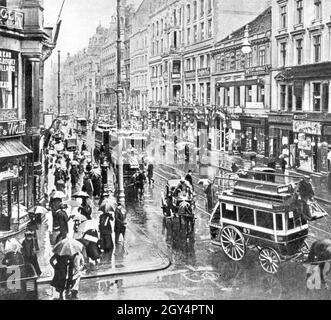 La photo montre la foule sur Leipziger Straße, à l'angle de Friedrichstraße à Berlin-Mitte en 1899.Des tramways électriques fonctionnent en arrière-plan, tandis que des calèches et un bus omnibus (direction Anhalter Bahnhof) sont également visibles au premier plan.Sur la gauche se trouve une branche du magasin de tabac Loeser et Wolff.[traduction automatique] Banque D'Images