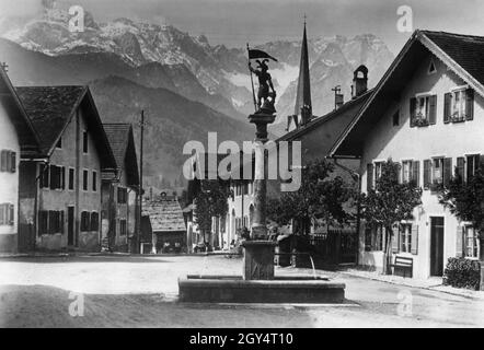 La photo montre le Floriansbrunnen à Floriansplatz à Garmisch-Partenkirchen (quartier de Partenkirchen) en 1931.En bas de la vallée, la Ballengasse mène à l'église paroissiale Maria Himmelfahrt, dont la flèche est visible sur la droite.Au loin se trouve le Höllental, entouré par Alpspitze, Höllentalspitzen, Zugspitze et Waxenstein.[traduction automatique] Banque D'Images